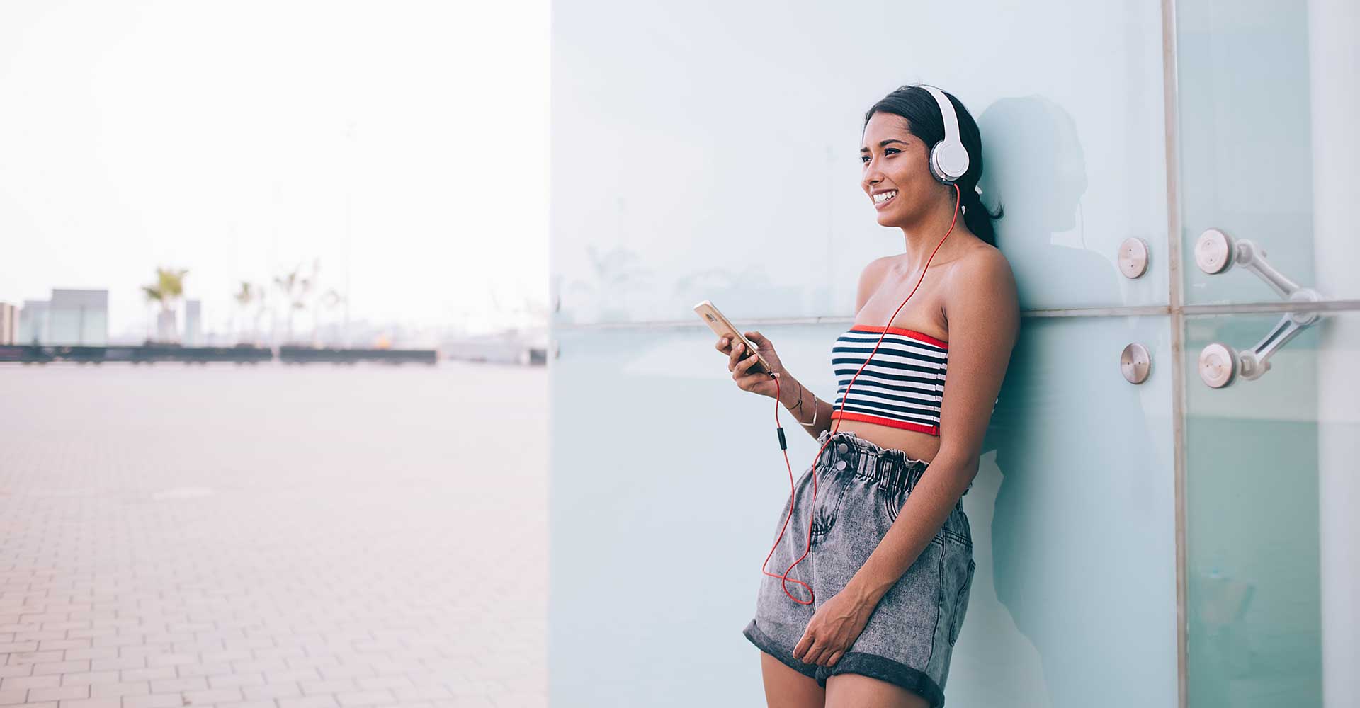 Image with hispanic girl listening to audio content on the go with smartphone and headset